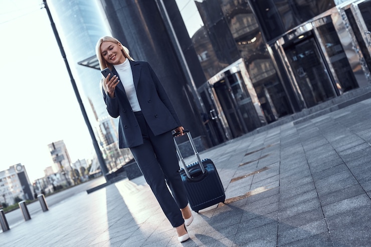 Foto retrato de cuerpo entero de una empresaria exitosa sonriente tirando de la maleta