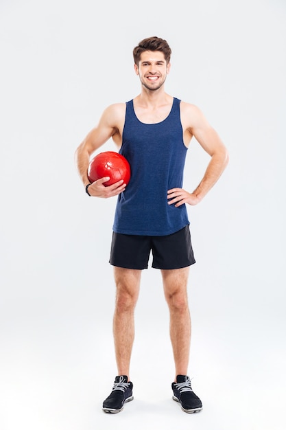 Retrato de cuerpo entero de un entrenamiento de hombre guapo con pelota de fitness aislado sobre un fondo gris