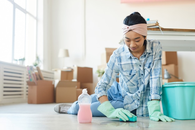 Retrato de cuerpo entero de feliz mujer asiática limpiando el piso en la nueva casa o apartamento después de mudarse