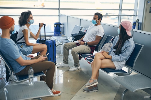 Retrato de cuerpo entero del grupo de turistas con equipaje en el aeropuerto sentado en el banco en la sala de embarque