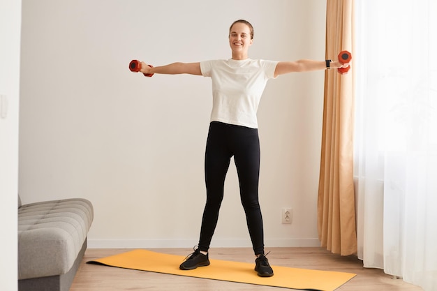 Retrato de cuerpo entero de una hermosa joven haciendo ejercicios con pesas mujer atlética con cuerpo perfecto entrenando bíceps y tríceps Fuerza y motivación