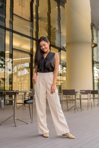 Retrato de cuerpo entero de hermosa mujer asiática al aire libre en el restaurante cafetería tiro vertical