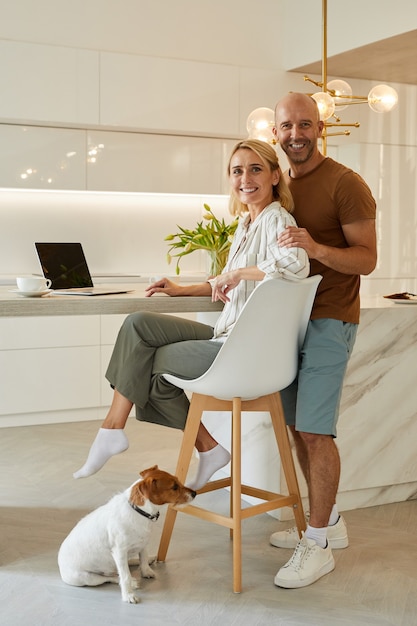 Retrato de cuerpo entero de la hermosa pareja adulta sentada en el mostrador de la cocina en el interior de una casa