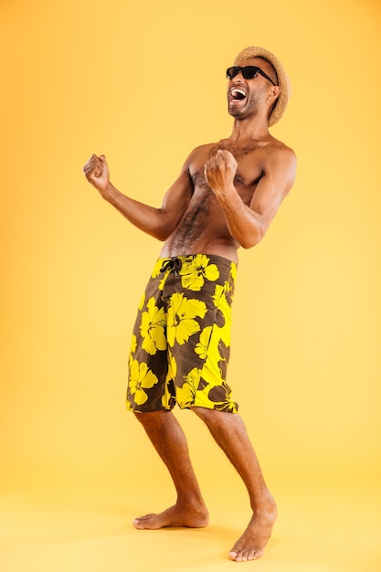 Retrato de cuerpo entero de un hombre afro feliz en traje de baño celebrando su éxito aislado en una pared naranja