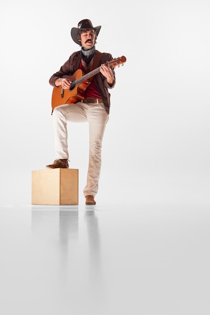 Retrato de cuerpo entero de un hombre con bigotes en ropa de estilo rústico tocando la guitarra aislada sobre