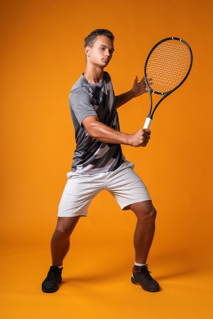 Retrato de cuerpo entero de un hombre jugador de tenis contra el fondo naranja