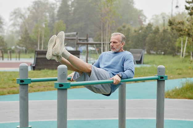 Retrato de cuerpo entero de un hombre maduro deportivo haciendo ejercicio en barras paralelas al aire libre copiando espacio