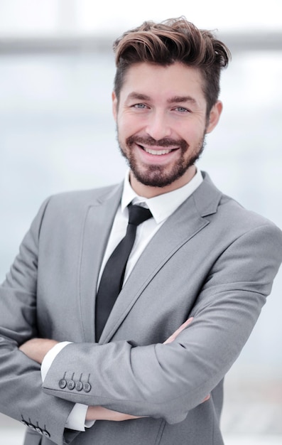 Retrato de cuerpo entero de un hombre de negocios sonriente con las manos cruzadas contra el fondo de la ventana