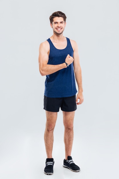 Retrato de cuerpo entero de un hombre sonriente mostrando sus bíceps aislado sobre un fondo gris