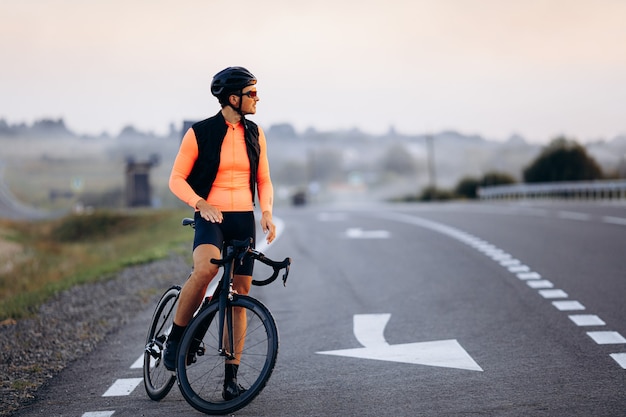 Retrato de cuerpo entero de joven ciclista en traje de deporte brillante montando bicicleta durante el tiempo de la tarde