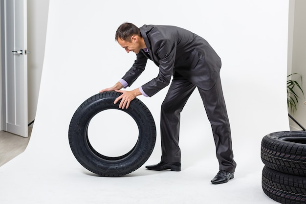 Foto retrato de cuerpo entero de un joven empresario apoyado en un montón de neumáticos de coche aislado sobre fondo blanco.