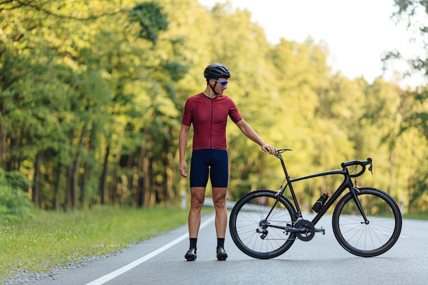 Retrato de cuerpo entero de un joven con piernas fuertes posando con su bicicleta negra