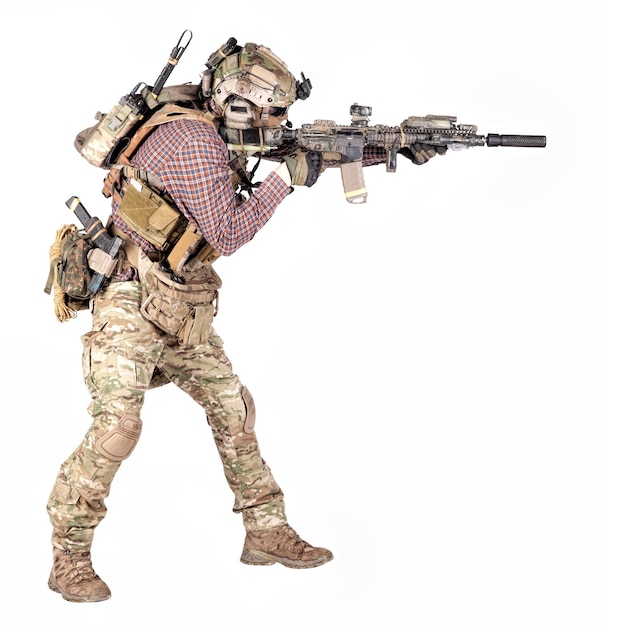 Retrato de cuerpo entero de un jugador de airsoft en camisa a cuadros, con uniforme de camuflaje, casco con auriculares de radio tácticos, armadura corporal, apuntando con un rifle de servicio, réplica de estudio, disparar aislado en blanco