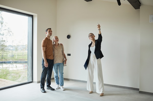 Retrato de cuerpo entero de una mujer agente de bienes raíces dando un recorrido por el apartamento a una pareja joven que compra una nueva propiedad, espacio de copia