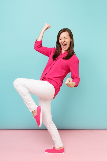 Retrato de cuerpo entero de mujer bonita joven sonriente en blusa camisa rosa, pantalón blanco posando aislado en la pared pastel azul rosa brillante.