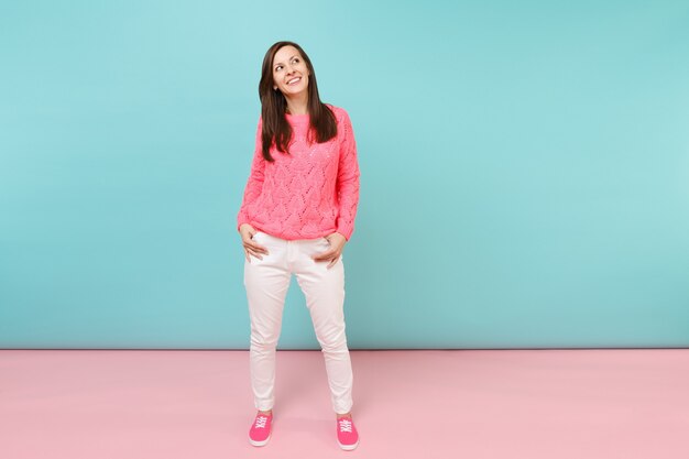 Retrato de cuerpo entero de una mujer joven soñadora en un suéter rosa de punto, pantalones blancos posando