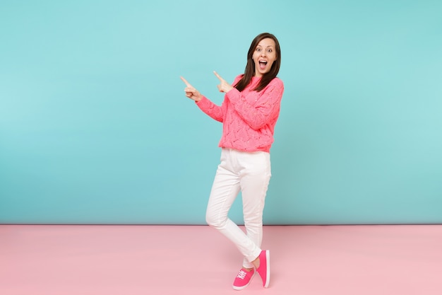 Retrato de cuerpo entero de mujer joven sonriente en suéter rosa de punto, pantalones blancos posando