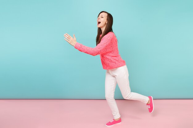 Retrato de cuerpo entero de mujer joven sonriente en suéter rosa de punto, pantalones blancos posando