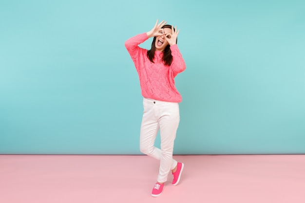 Retrato de cuerpo entero de mujer joven sonriente en suéter rosa de punto, pantalones blancos posando