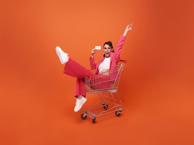Retrato de cuerpo entero de mujer de moda sonriente feliz con carrito y mostrando tarjeta de crédito