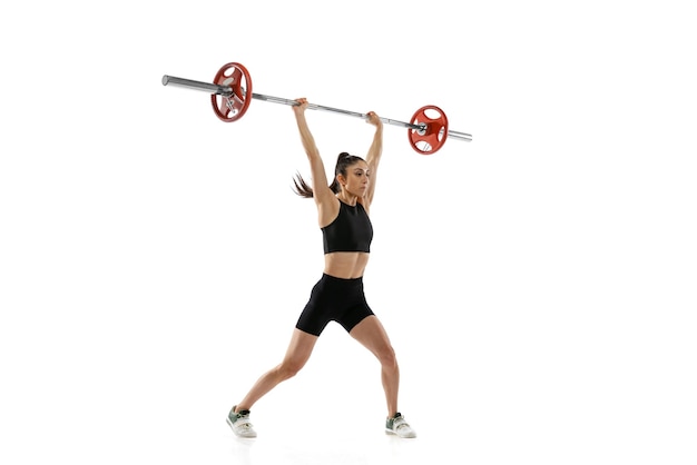 Retrato de cuerpo entero de mujer musculosa en ropa deportiva haciendo ejercicio con una barra de peso aislada sobre fondo blanco Concepto de levantamiento de pesas deportivo