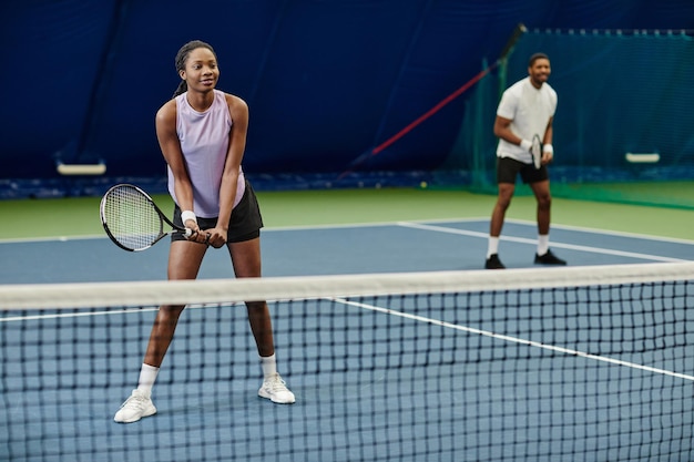 Retrato de cuerpo entero de una mujer negra sonriente jugando al tenis en el espacio de copia de la cancha interior