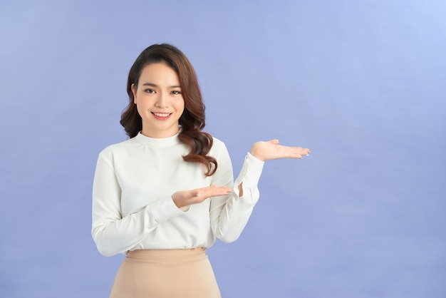 Retrato de cuerpo entero de una mujer pensativa feliz sosteniendo copyspace en la palma aislada sobre un fondo púrpura