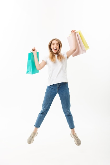 Retrato de cuerpo entero de una niña bonita feliz sosteniendo bolsas de la compra mientras salta y mira a cámara aislada sobre fondo blanco.