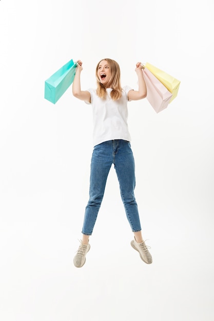 Retrato de cuerpo entero de una niña bonita feliz sosteniendo bolsas de compras mientras salta