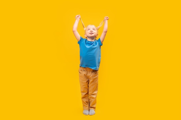 Retrato de cuerpo entero de una niña con dos colas de caballo mirando hacia arriba Feliz niño en edad preescolar en camiseta azul sobre fondo amarillo