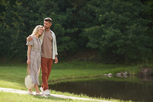 Retrato de cuerpo entero de la romántica pareja adulta abrazándose mientras camina hacia el lago en un hermoso paisaje natural