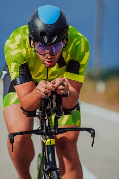 Retrato de cuerpo entero de un triatleta activo en ropa deportiva y con casco protector andando en bicicleta. Enfoque selectivo.