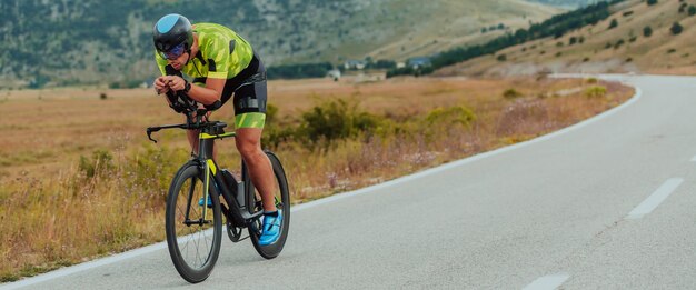 Retrato de cuerpo entero de un triatleta activo en ropa deportiva y con casco protector andando en bicicleta. Enfoque selectivo.