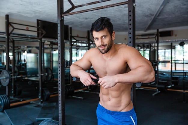 Retrato de un culturista masculino mucular descansando cerca de barras paralelas en el gimnasio