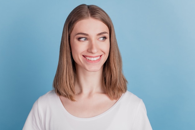 Retrato de curiosa chica impresionante mirar lado espacio vacío sonrisa con dientes sobre fondo azul.