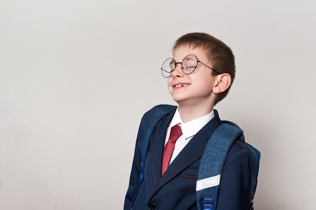 Retrato de un curioso colegial en un traje, gafas y una mochila.