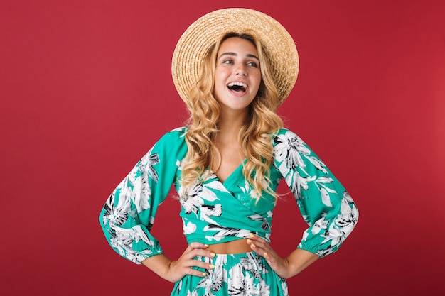 Retrato de cutie riendo feliz joven hermosa rubia linda mujer en vestido posando aislado sobre pared roja mirando a un lado