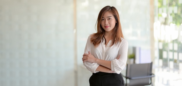 Retrato da bela empresária asiática em pé na sala de escritório e sorrindo para a câmera