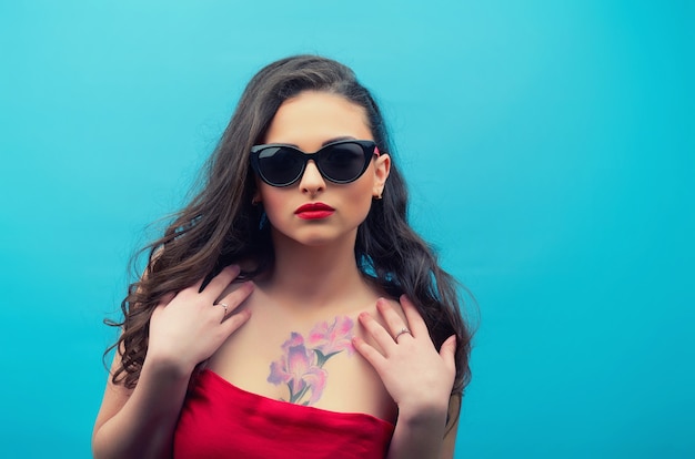 Retrato da bela jovem de óculos no vestido vintage vermelho na parede azul. jovem modelo feminino.