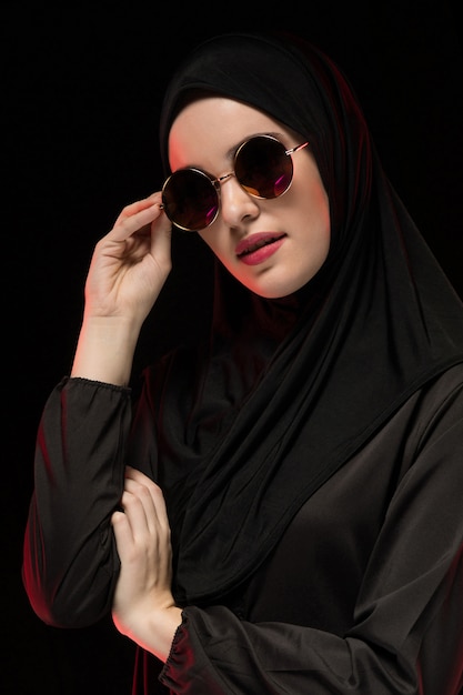 Retrato da bela jovem muçulmana elegante vestindo preto hijab e óculos de sol como conceito de moda oriental moderna posando preto