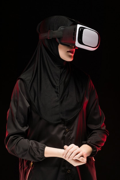 Retrato da bela jovem muçulmana inteligente vestindo preto hijab usando fone de ouvido de realidade virtual