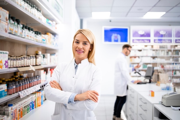 Retrato da bela loira farmacêutica feminina em pé na loja da farmácia perto da prateleira com medicamentos.