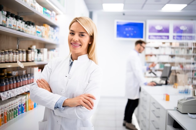 Retrato da bela loira farmacêutica feminina em pé na loja da farmácia perto da prateleira com medicamentos.