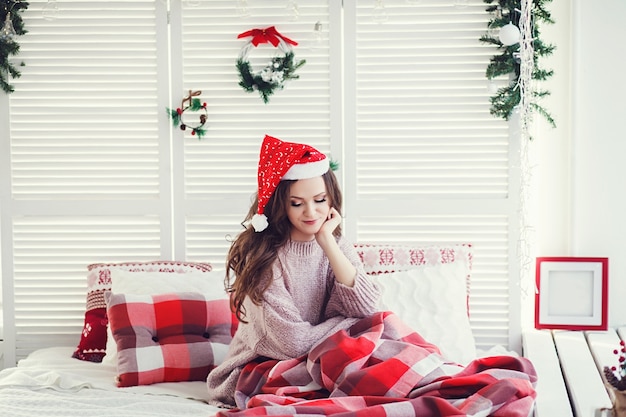 Retrato da bela modelo feminino com chapéu de Papai Noel na cama. conceito de natal