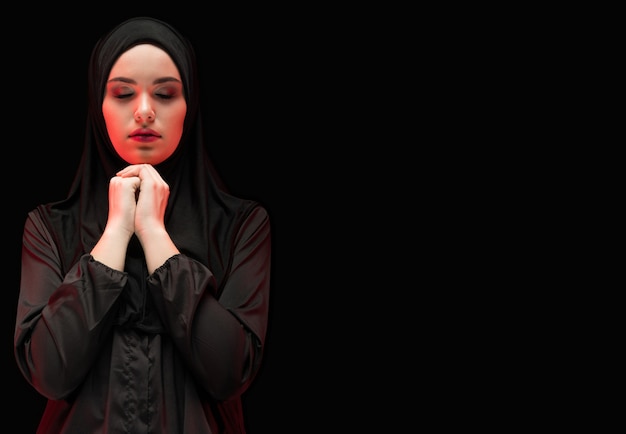 Retrato da bela mulher muçulmana séria vestindo preto hijab com os olhos fechados como rezar conceito com copyspace