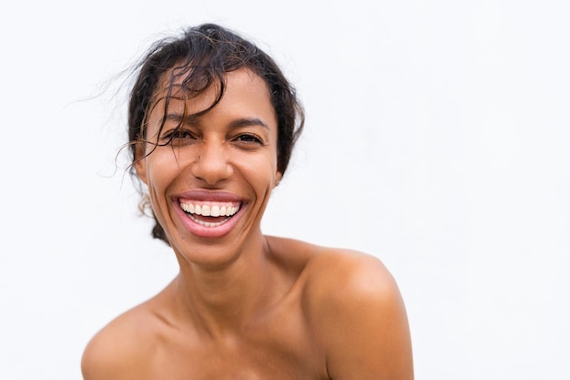Retrato da beleza da jovem mulher afro-americana em topless com ombros nus em fundo branco com pele perfeita e maquiagem natural rindo positivo
