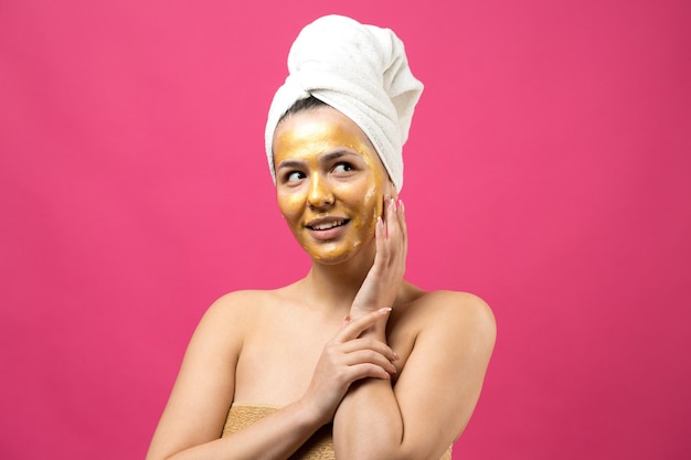 Retrato da beleza da mulher na toalha branca na cabeça com máscara nutritiva de ouro no rosto Skincare limpeza eco spa cosmético orgânico relax conceito