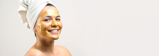 Retrato da beleza da mulher na toalha branca na cabeça com máscara nutritiva de ouro no rosto Skincare limpeza eco spa cosmético orgânico relax conceito