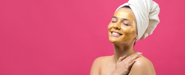 Retrato da beleza da mulher na toalha branca na cabeça com máscara nutritiva de ouro no rosto Skincare limpeza eco spa cosmético orgânico relax conceito