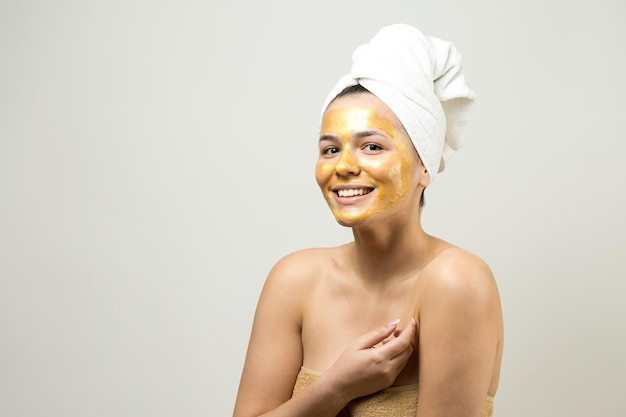 Retrato da beleza da mulher na toalha branca na cabeça com máscara nutritiva de ouro no rosto Skincare limpeza eco spa cosmético orgânico relax conceito